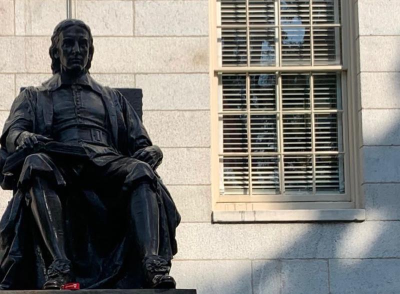 This is a picture of the top of the John Harvard Statue, which shows only the shape of the statue itself, and not the base with it's description. The statue shows a man posing in a sitting, very academic looking, position. 