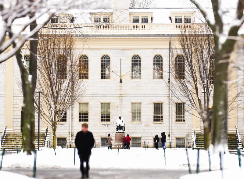 A winter landscape showing Harvard's University Hall framed by snow-covered trees.