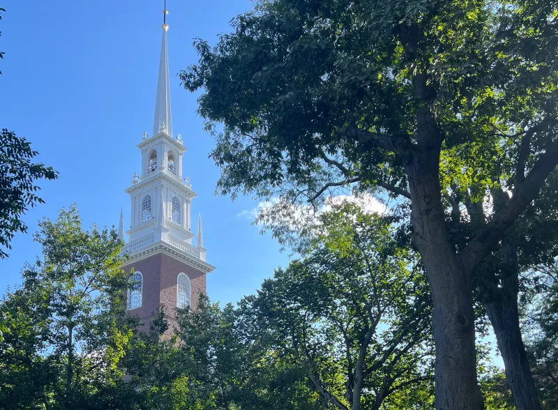 White steeple and brick exterior of Memorial Church framed by lush green trees.