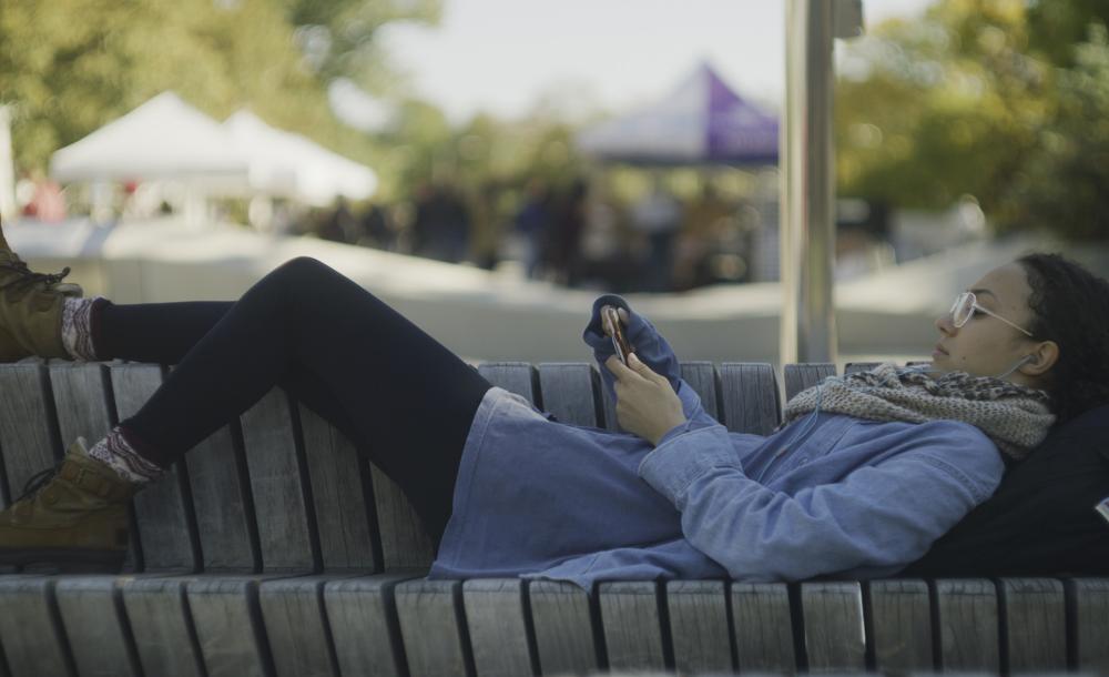 Student laying on bench at Science Center Plaza with her phone