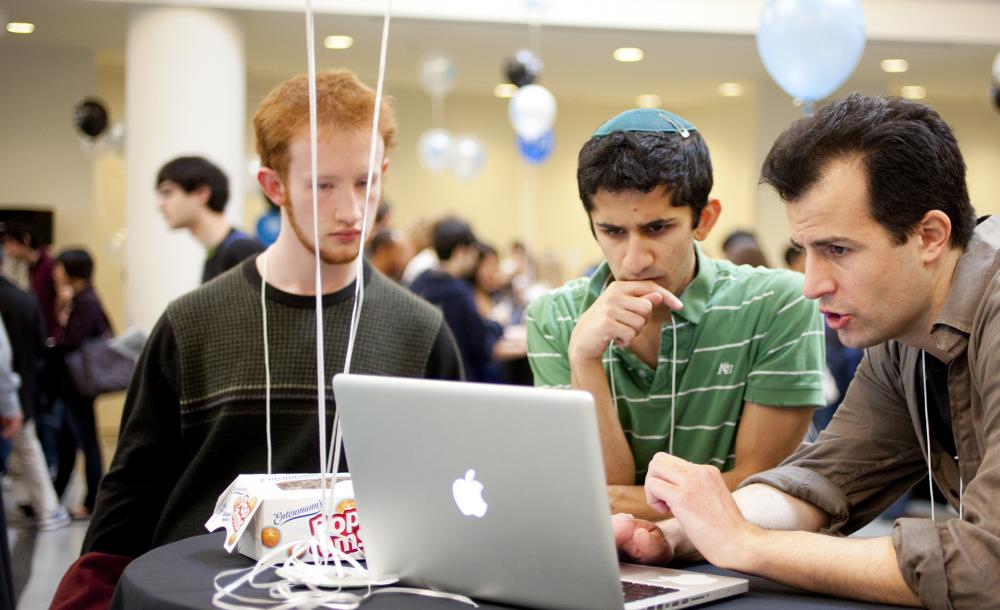3 students in front of a laptop at a tech fair