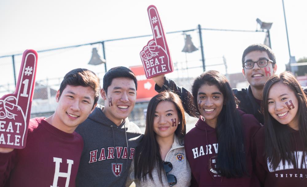 Six Harvard students with foam fingers cheering for Harvard-Yale football game