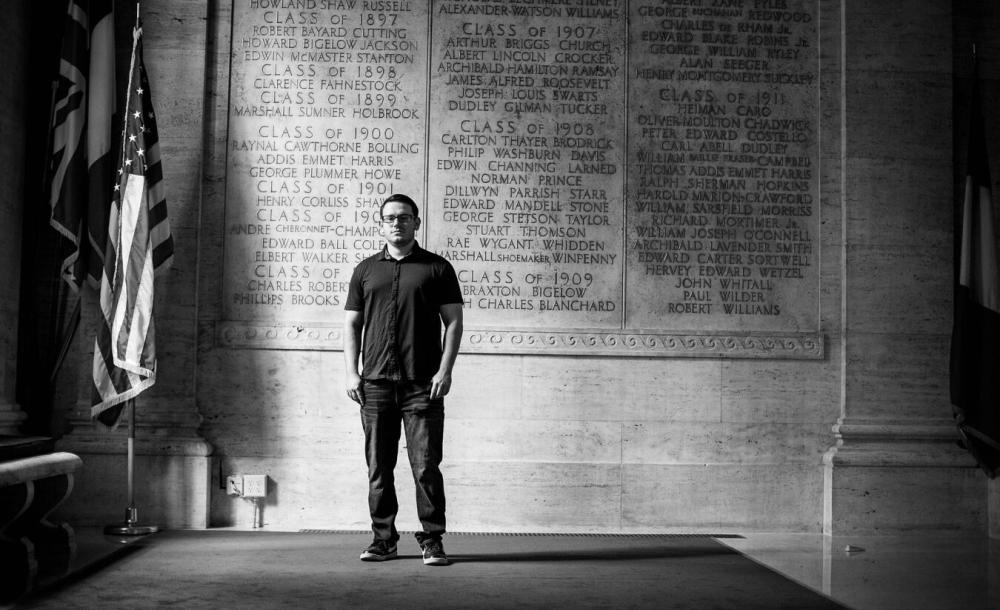 James stands in front of a wall etched with names of Harvard veterans
