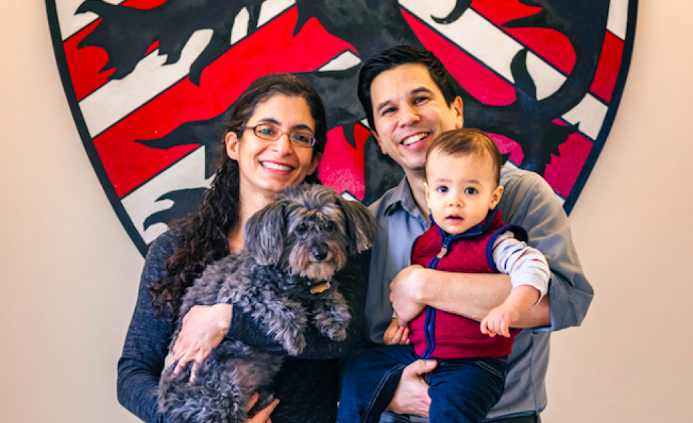 A portrait of Kiran Gajwani and Stephen Chong, faculty deans of Winthrop House, with their son and dog.