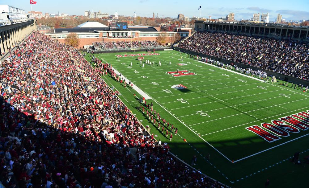 An upward view of Harvard Stadium filled with fans and football action on the field.