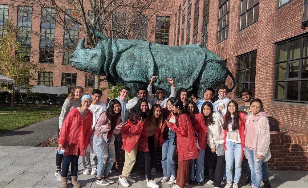 Students in white and red lab coats standing in front of a rhino statue.