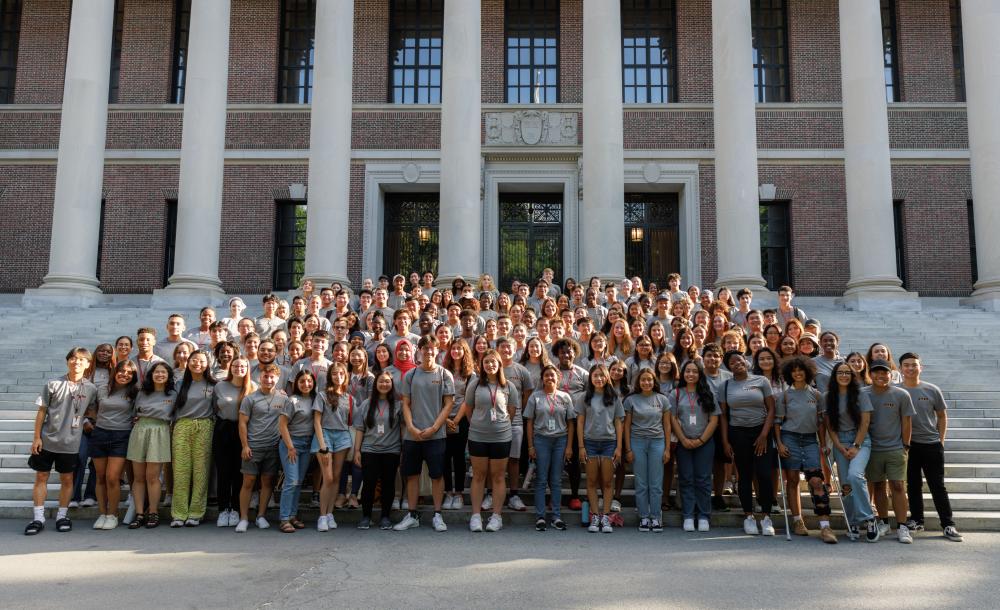 A large group of students gather in front of a library to pose for a picture. 