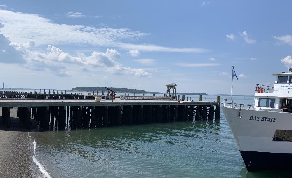 Picture of pier stretching out into the ocean with a white boat coming in.