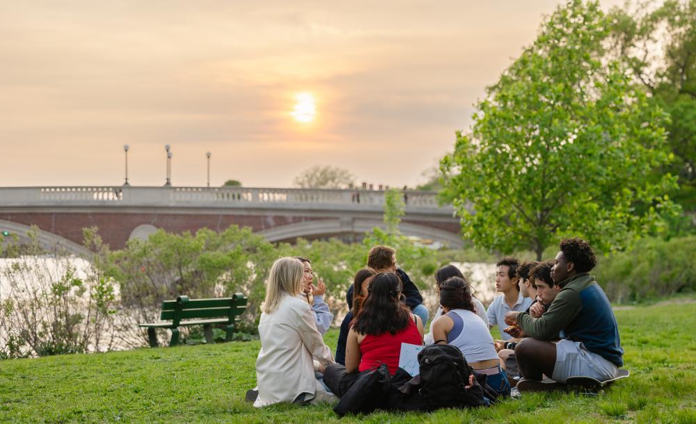 A group of several students sitting on the bank of the Charles River.