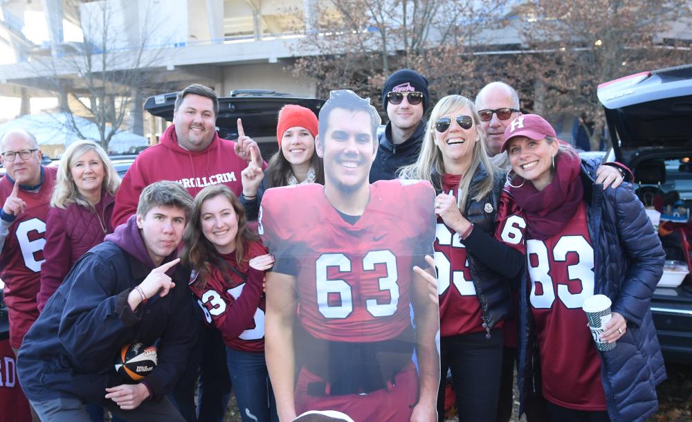 students tailgating outside of football game. they are holding a cardboard cutout of one of the players