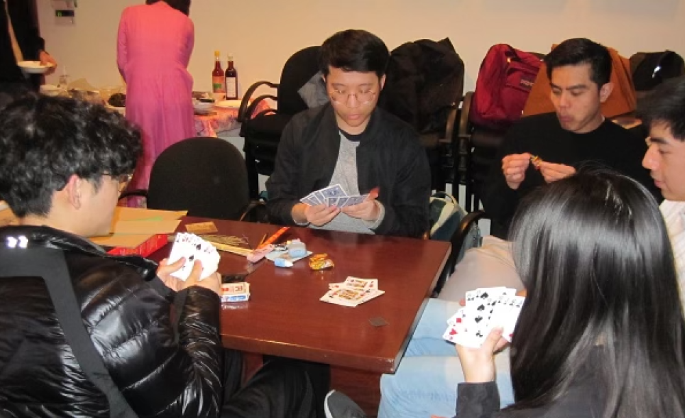 A group of five people playing cards at a table.