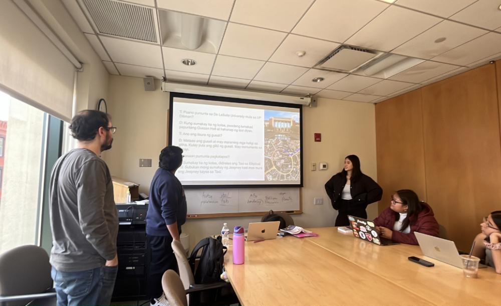 Students sitting and standing around a table looking at a presentation