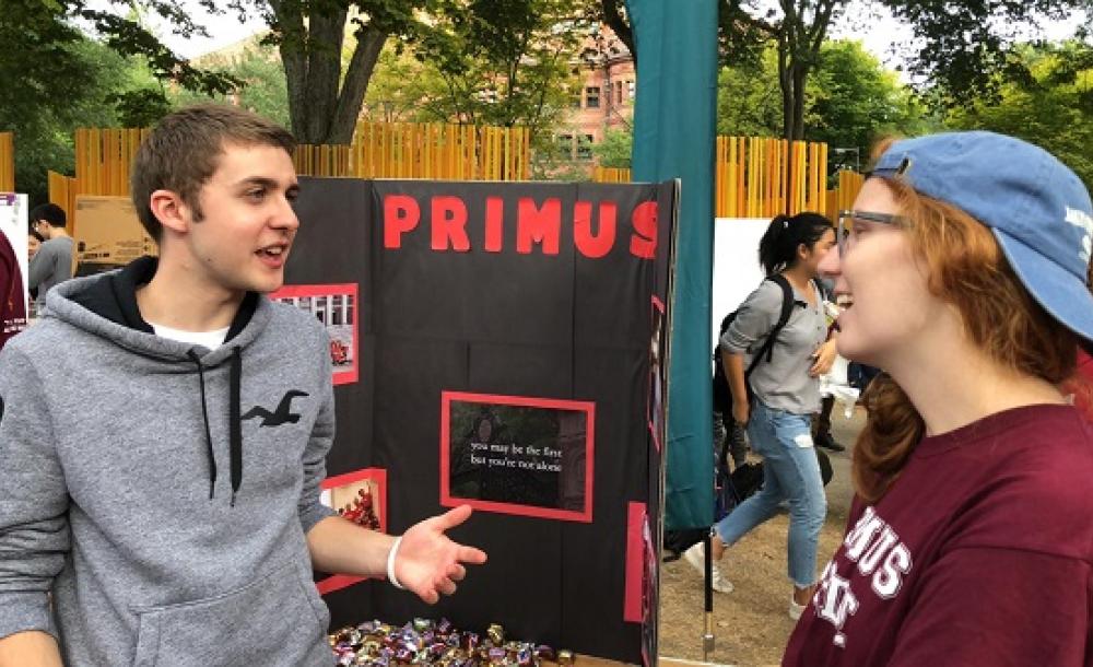 two people talking outside next to a poster that says Primus
