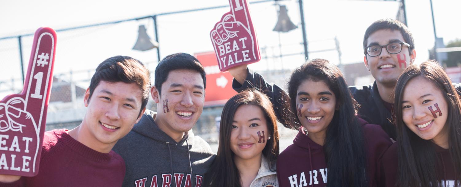 Six Harvard students with foam fingers cheering for Harvard-Yale football game