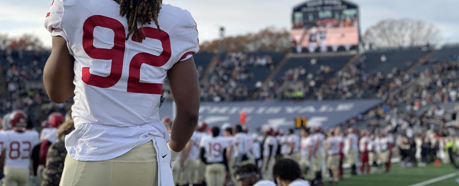 A student athlete watches his teammates on the sidelines during the final moments of the 2021 Harvard-Yale game.