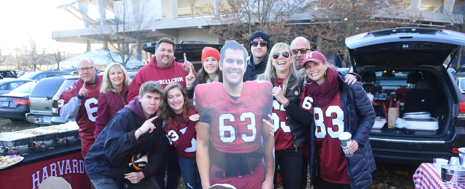 students tailgating outside of football game. they are holding a cardboard cutout of one of the players