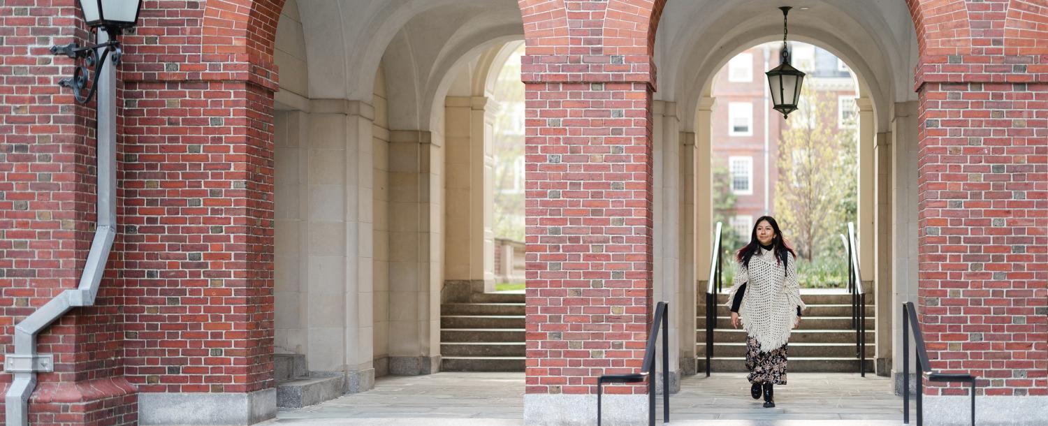 Student walking through the courtyard arches of a House with her backpack.