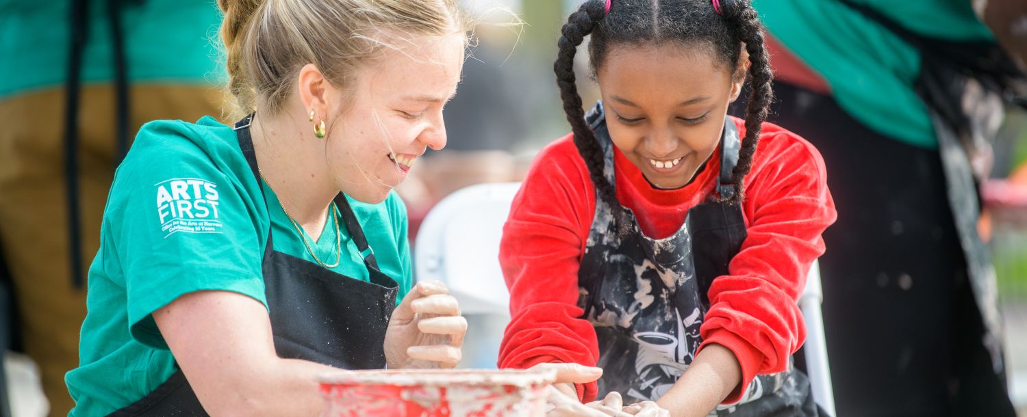 Smiling woman and child working with clay at a pottery wheel.