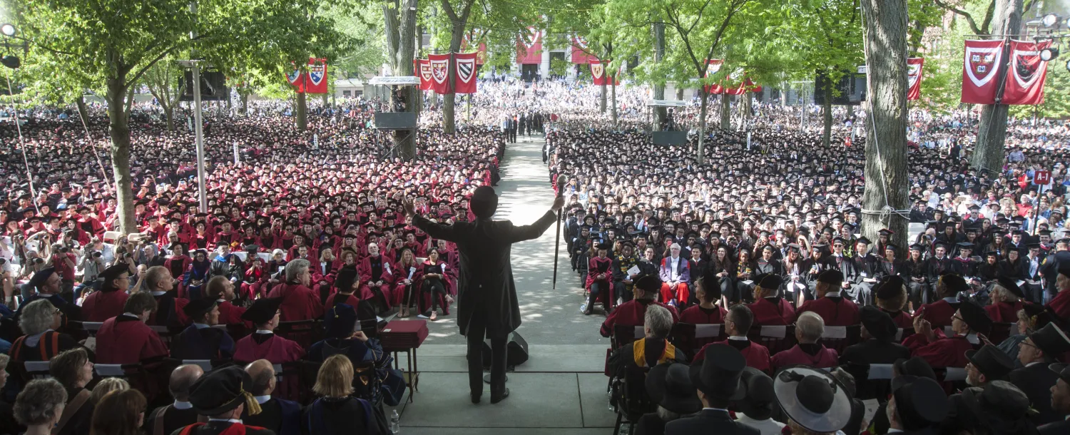Speaker addressing a large crowd at an outdoor graduation ceremony