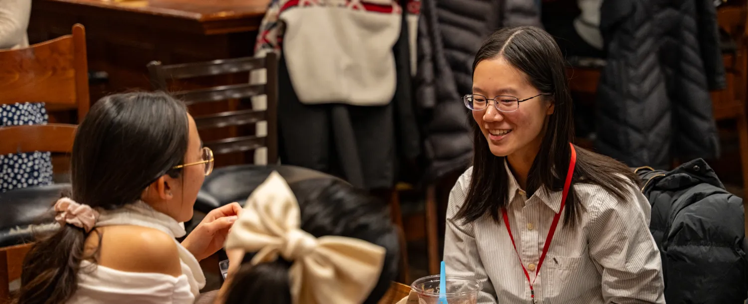 3 girls seated at a table talking in conversation.