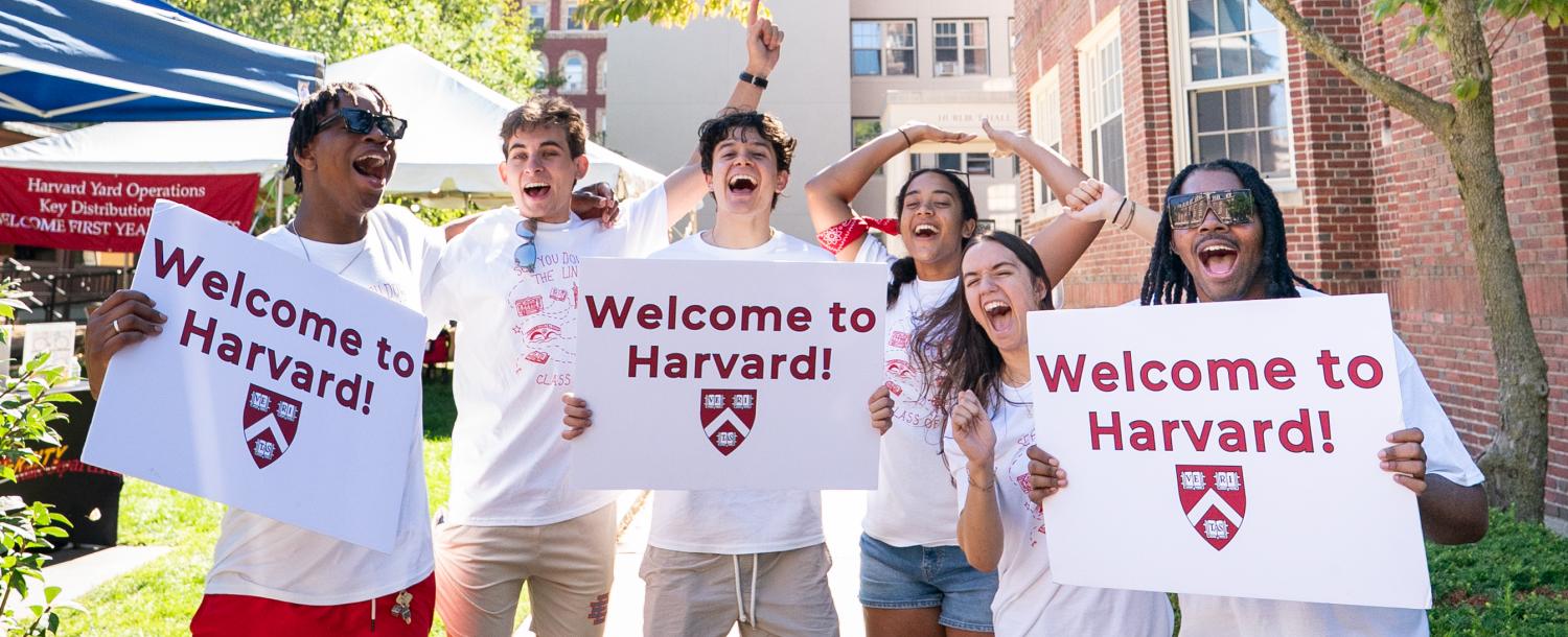 Harvard College students smile while holding "Welcome to Harvard" signs to welcome the incoming class on move-in day.
