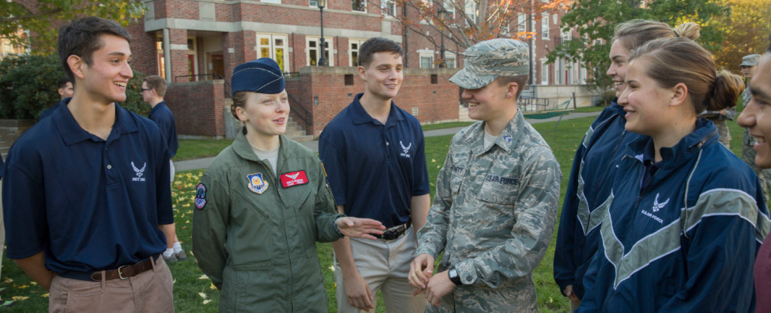 A group of Air Force cadets stand and talk outside on a campus lawn.