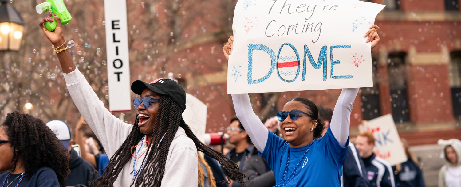 Students holding up a sign for Eliot House that reads "they're coming dome".
