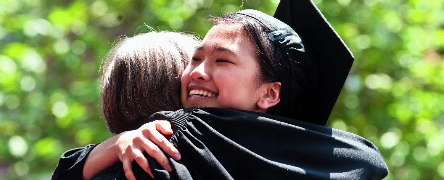 2 individuals in commencement regalia hugging