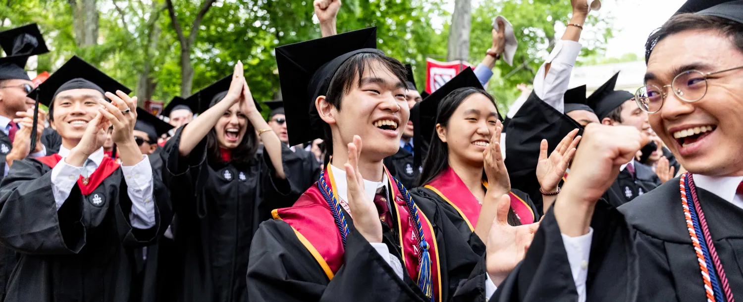 Students cheering in the crowd while wearing their regalia at Commencement.