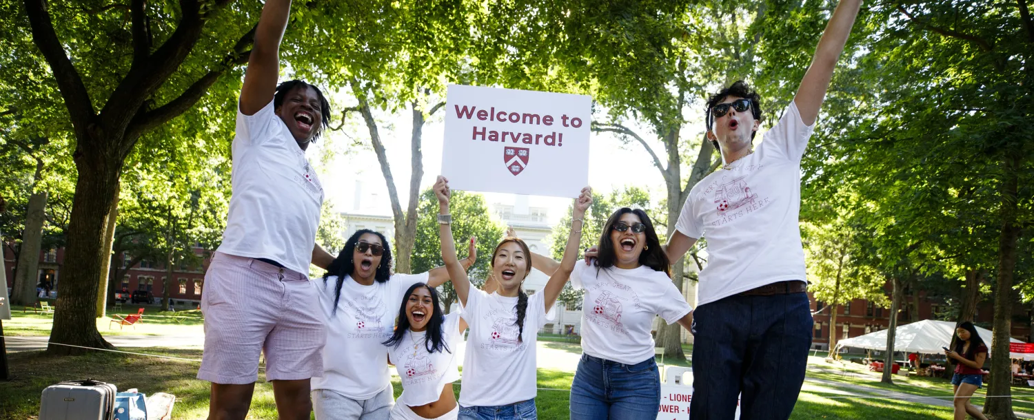 A group of five students cheering with a Welcome to Harvard sign.