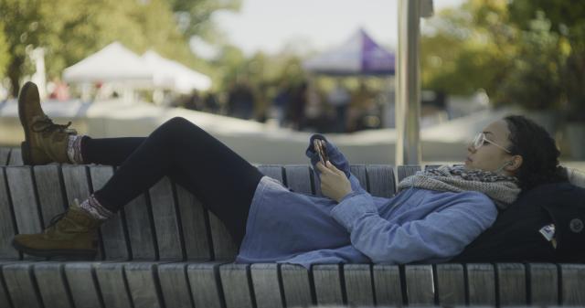 Student laying on bench at Science Center Plaza with her phone