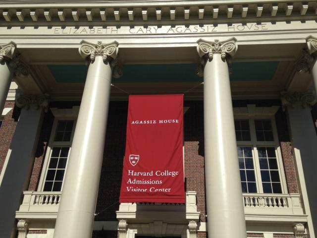 A picture of Agassiz House, taken during my first visit to Harvard. There is a big red banner that hangs between the white columns of the building and reads,"Agassiz House Harvard College Admissions Visitor Center." 