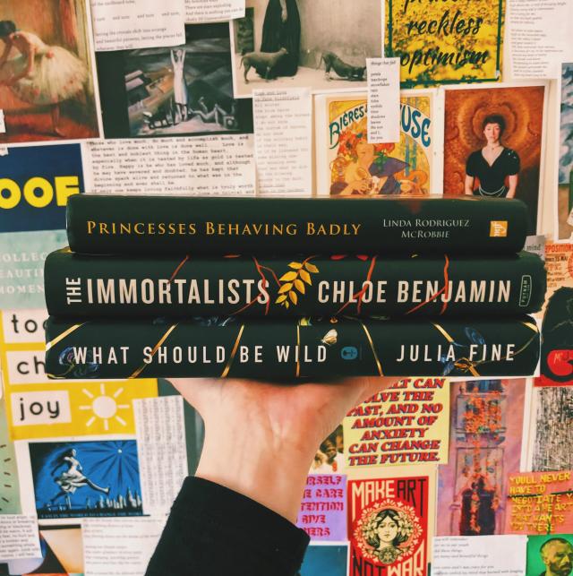 A stack of books held in front of a decorated wall.