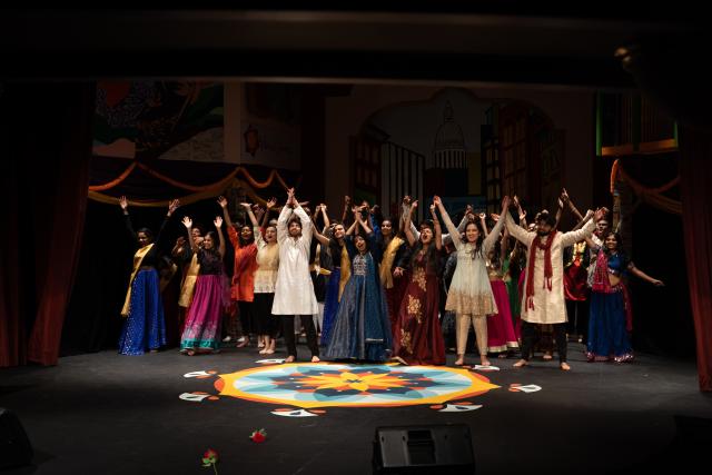 Students wearing South Asian clothing all preparing to bow on stage in the finale of Harvard Ghungroo 2020, with a Rangoli set in front of them.