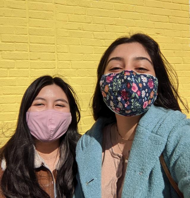 Two girls standing in front of a yellow wall.