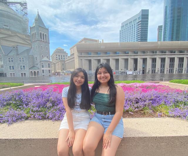 Two girls sitting by flower beds.