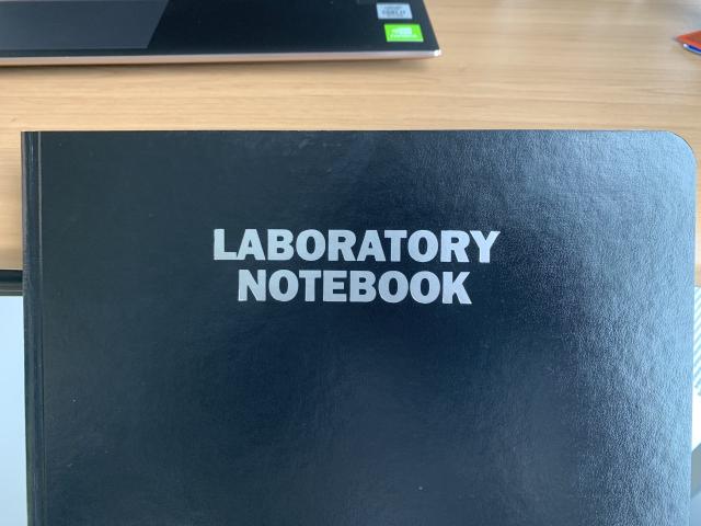 A black notebook with the words "LABORATORY NOTEBOOK" in white at the center.