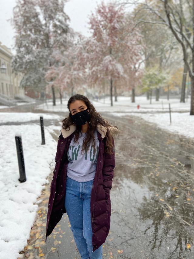 Girl in a big dark red coat in a park while it is snowing. 