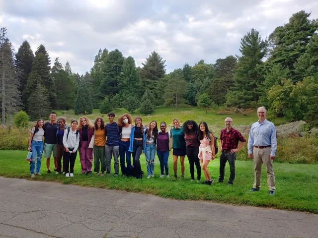 Group picture of students and professors standing beside a road with trees in the background.