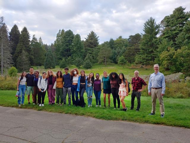 Group picture of students and professors standing beside a road with trees in the background.