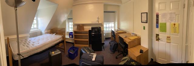 Picture of a dorm room with luggage and unorganized furniture.