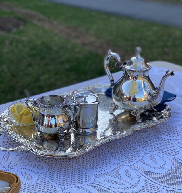 A picture of a silver teapot, creamer pitcher, sugar container, and bowl of lemons on a silver platter.