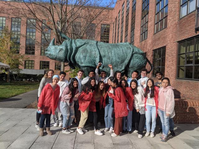 Students in white and red lab coats standing in front of a rhino statue.