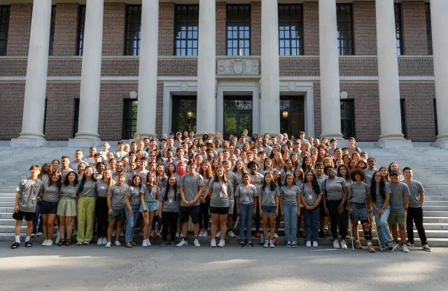 A large group of students gather in front of a library to pose for a picture. 