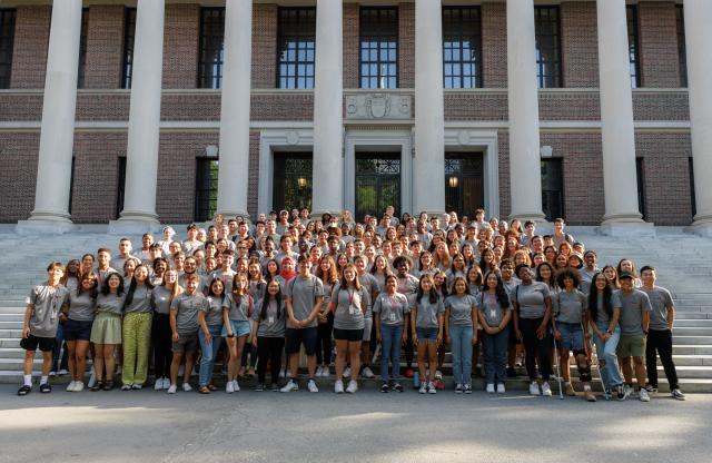 A large group of students gather in front of a library to pose for a picture. 