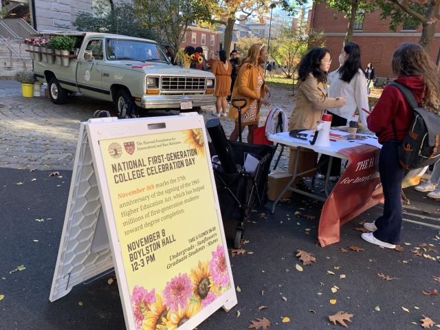Picture of "National First-Generation College Celebration" sign with students and a truck in the background.