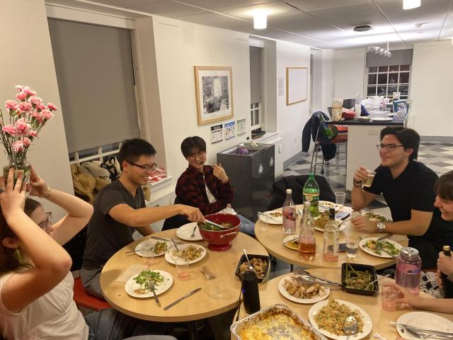 A group of friends sitting around dinner tables, some posing for the picture and some being extra silly for the picture. 