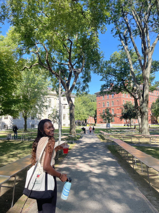 Author walking through Harvard Yard with hibiscus drink, smiling. 