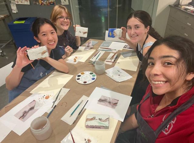 Four students smiling and surrounding a table with artworks