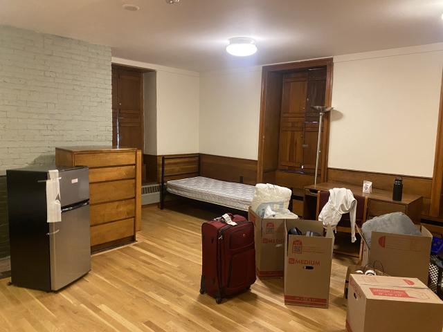 A picture of a room during move in day, with suitcases and boxes along with the furniture. The room, undecorated, looks new.